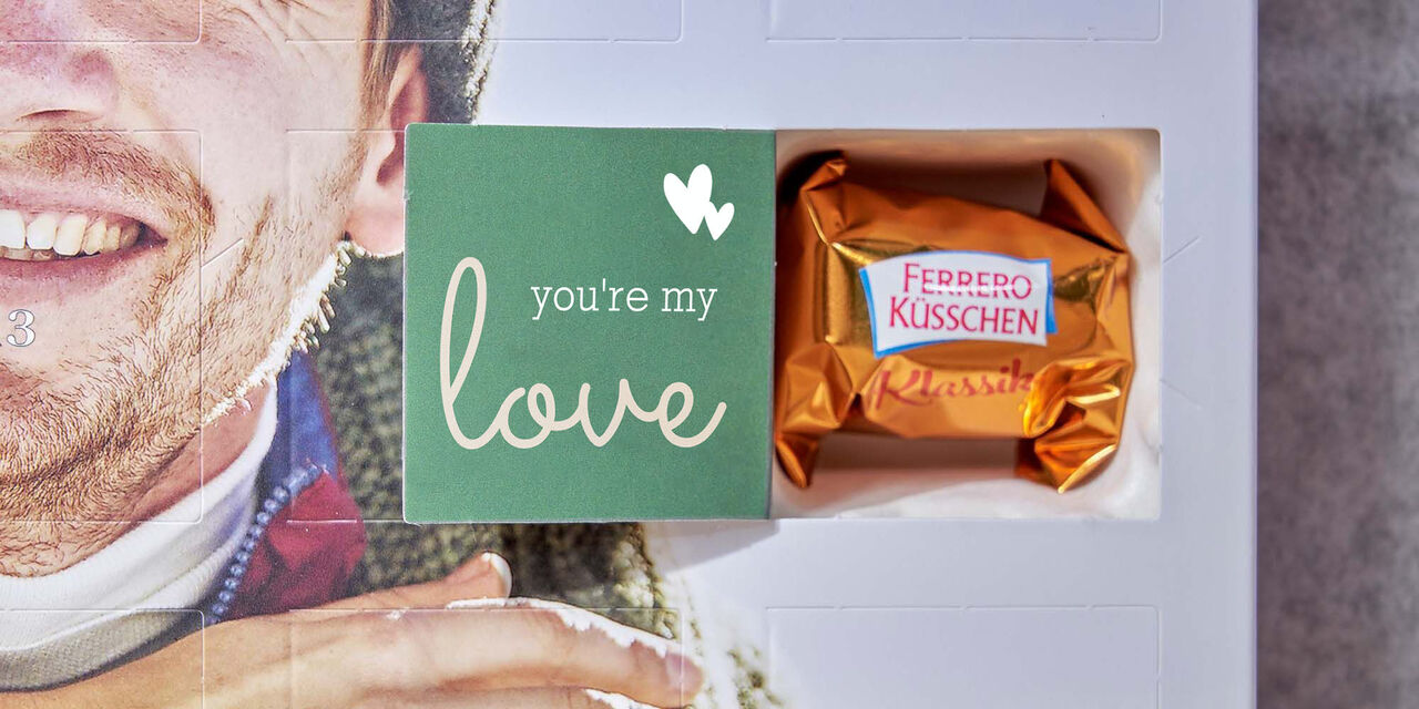 Na notranji strani odprtega okenca na adventnem koledarju piše "Ljubim te". Zraven sta vidna dva majhna srčka. Za vrati je Ferrerova čokoladica.